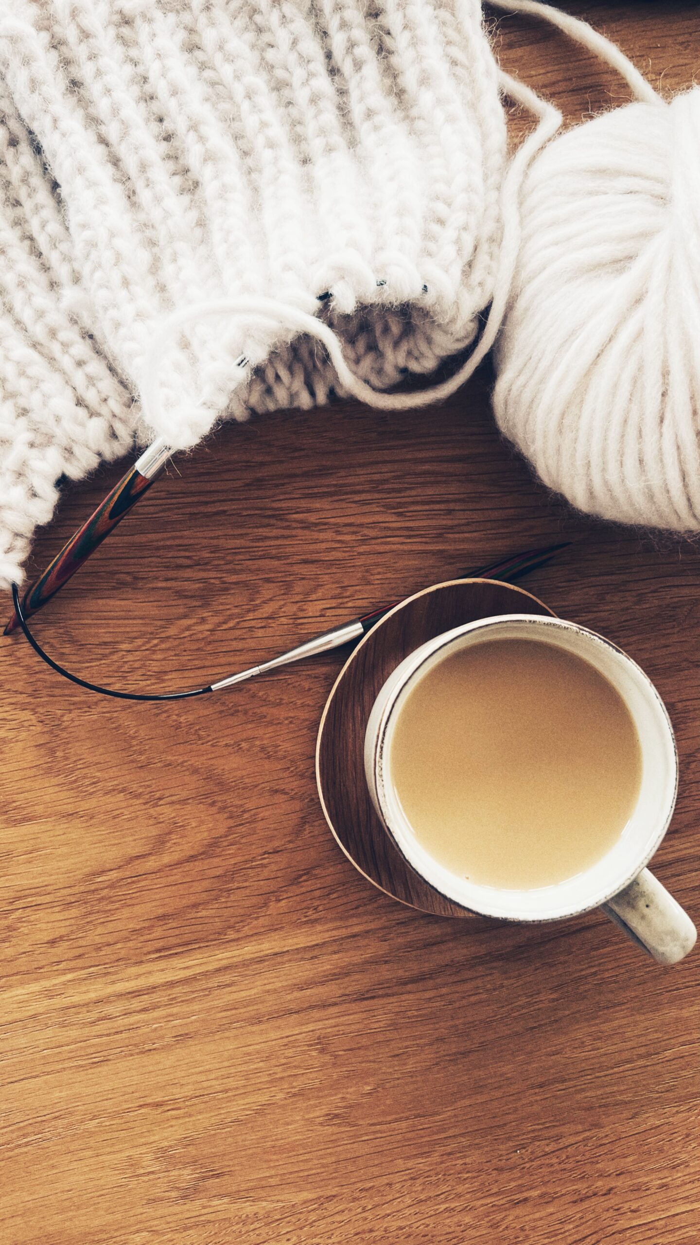 white coffee, wooden needles and wool on the wooden table durning cozy, autumn afternoon at home